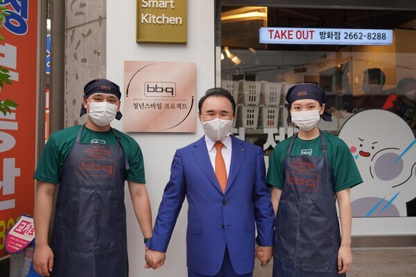 제너시스BBQ&nbsp;윤홍근 회장(가운데)이 지난 1일 서울 강서구 방화동로에 위치한 ‘청년 스마일 프로젝트’ 1호점 오픈 기념식에 참석해 가맹점주와 기념촬영을 하고 있다. / 사진=제너시스BBQ